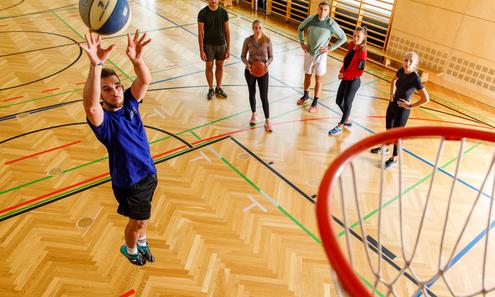 Sportler wirft Ball in Basketballkorb. Andere Sportler schauen zu