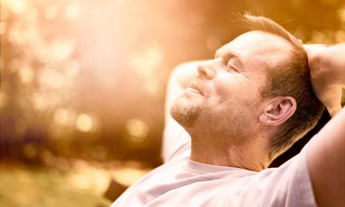 Ein Mann verschränkt seine Arme hinter dem Kopf und blickt zufrieden lächelnd mit geschlossenen Augen noch oben