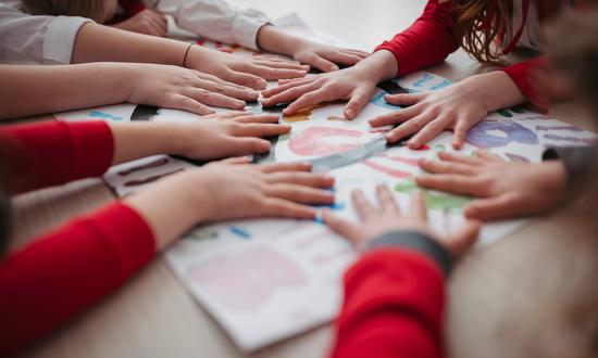 Kinderhände treffen sich auf einem bunten Blatt am Tisch