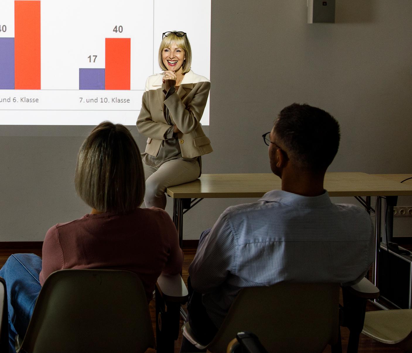 Lächelnde Professorin und zwei Studierende während einer Vorlesung