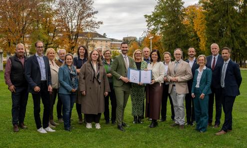 Gruppenfoto der Vertreter:innen auf einer Wiese, mit unterzeichnetem Papier in der Hand