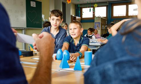 Schüler sitzen an einem Tisch und hören einem Lehrer zu.