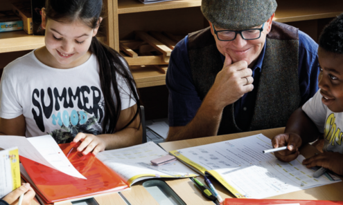 Lehrer, Schüler und Schülerin sitzend arbeitend und gut gelaunt am  Tisch