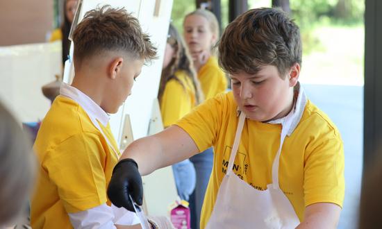 Zwei Schüler in Schürzen und Schutzhandschuhen zeigen ihr Experiment