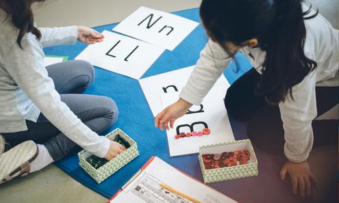 2 Kinder sitzen auf dem Boden und spielen mit Buchstaben