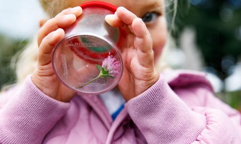 kleines Mädchen blickt in ein Glas mit Blume