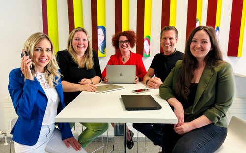 5 Personen sitzen um einen Tisch und lächeln