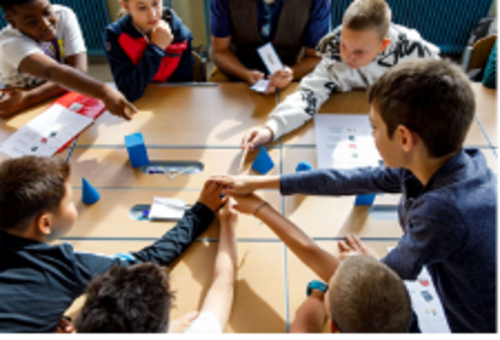 Kinder sitzen um einen Tisch und reichen die Hände in die Mitte